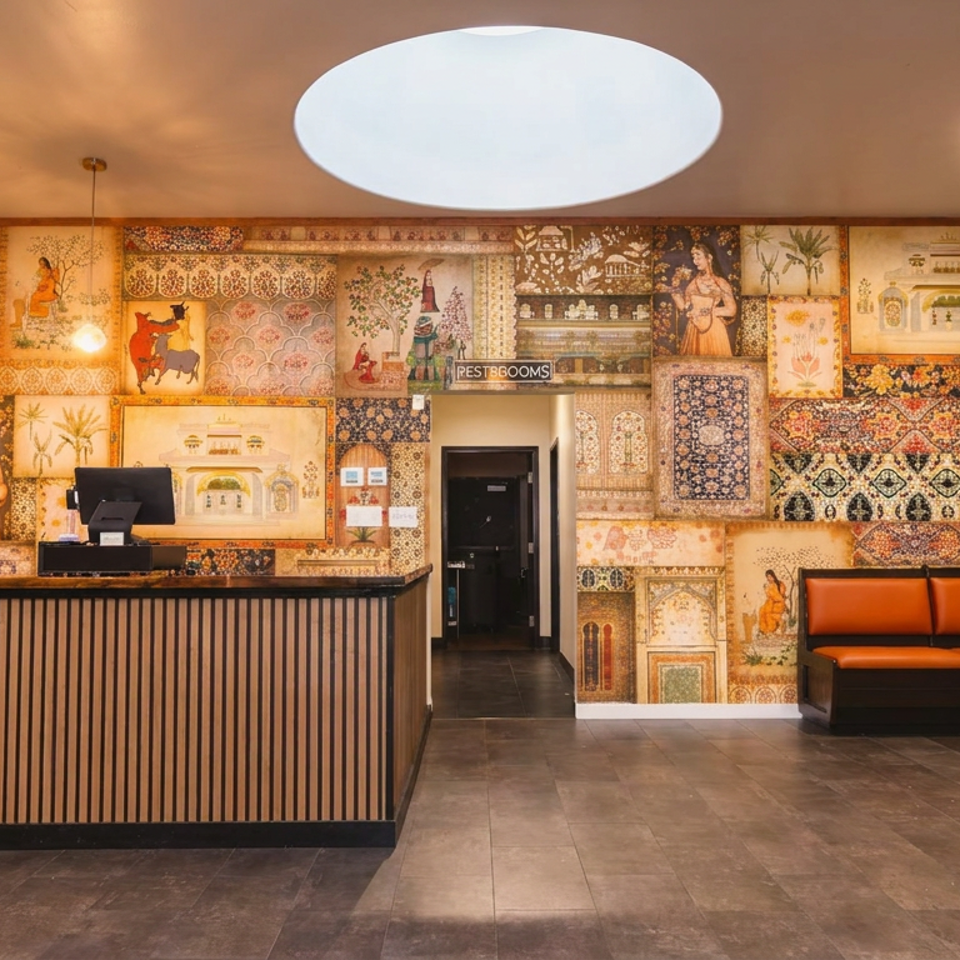 Restaurant lobby featuring a patterned mural wall, reception desk, orange banquette seating, and green dining chairs.