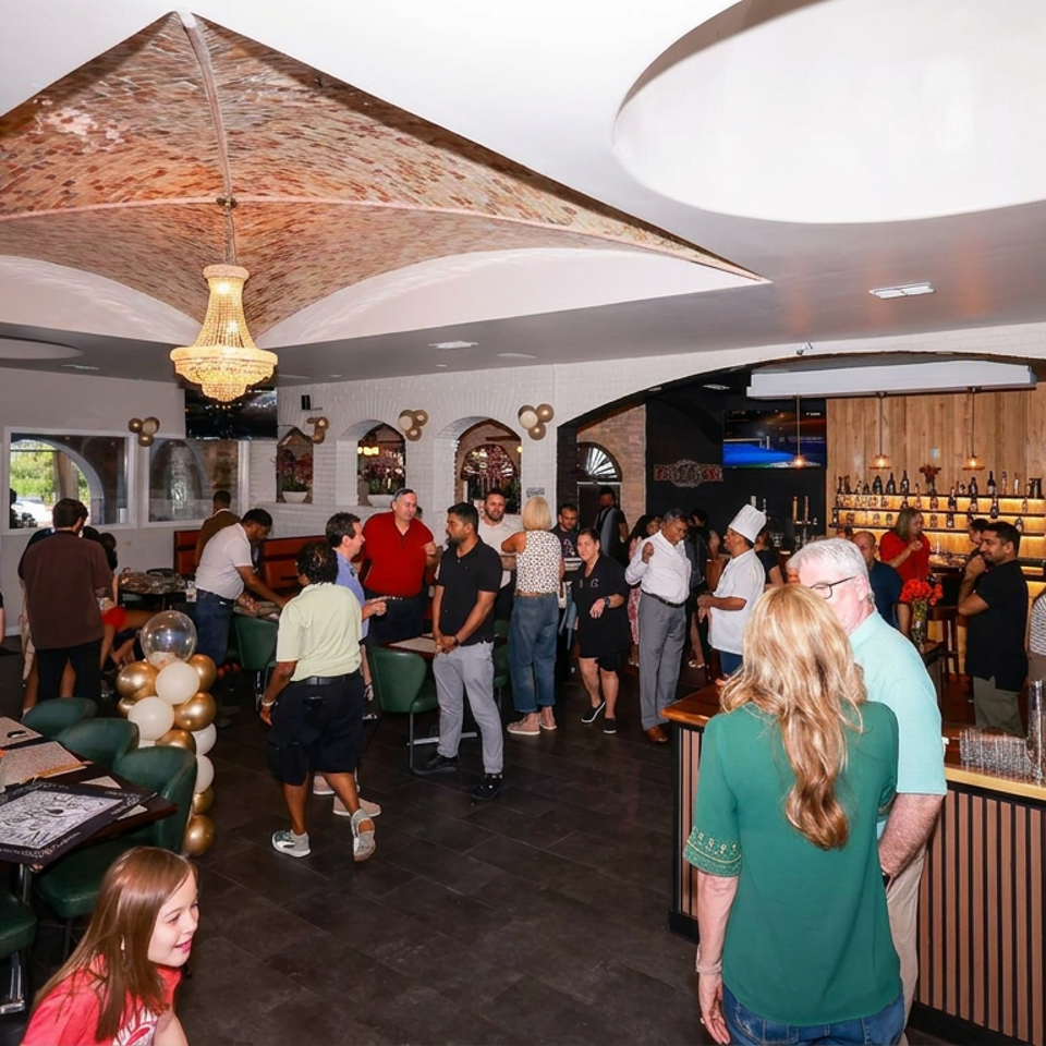 Bustling restaurant interior with diners, bartenders, green seating, decorative lighting, balloon arrangements, and a stocked bar.
