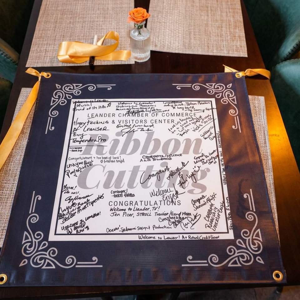 Restaurant table displays a framed congratulations certificate covered in signatures, surrounded by teal chairs, gold ribbons, and a rose centerpiece.